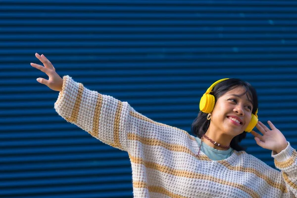 Ασιάτισσα Που Ακούει Μουσική Κίτρινα Ακουστικά Μπλε Φόντο Κολεγίου — Φωτογραφία Αρχείου