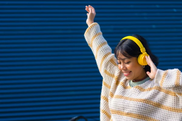 Ασιάτισσα Που Ακούει Μουσική Κίτρινα Ακουστικά Μπλε Φόντο Κολεγίου — Φωτογραφία Αρχείου