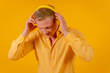 Sarı arka planda, kablosuz kulaklıklı, müzik dinleyen ve dans eden beyaz bir sarışın.