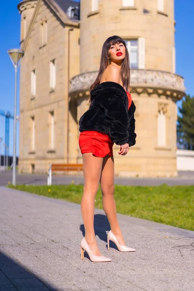 穿着红色衣服 穿着漂亮城堡的年轻女人 穿着黑色夹克 摆出一副时髦的姿势 面带微笑 — 图库照片