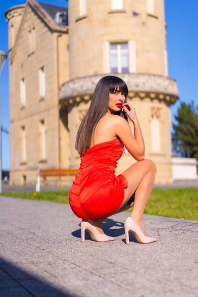 Young woman in a red dress in a beautiful castle, crouching in a fashion pose and smiling