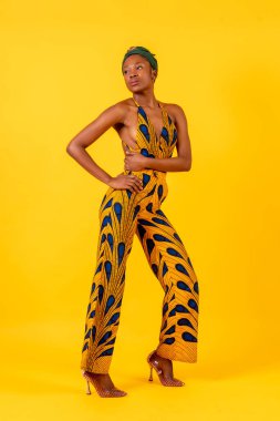 Stüdyoda sarı arka planda Afrikalı genç bir kadın, geleneksel kostümlü bir portre.