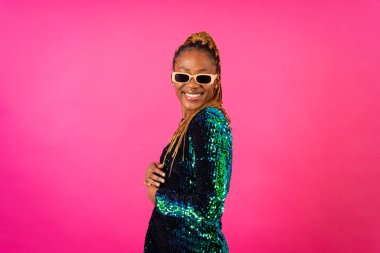 Örgü örgülü zenci bir kadın pembe arka planda dans ediyor, eğleniyor.