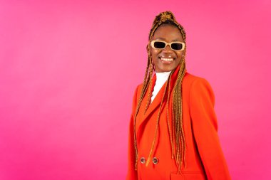 Pembe arka planda örgü ören Afrikalı genç bir kadın. Stüdyoda kırmızı elbiseli ve güneş gözlüklü bir portre.