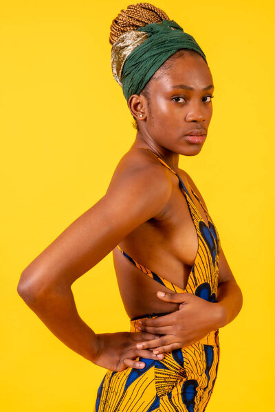 African young woman in the studio on a yellow background, traditional costume, serious look