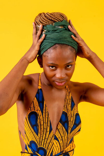 African young woman in traditional dress on yellow background, with green turban