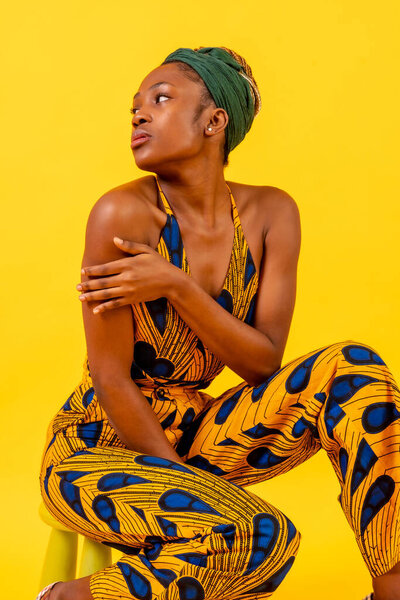 African young woman in traditional dress on yellow background, sitting in studio