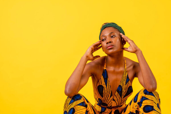 A woman of black ethnicity with traditional dress on a yellow background, sitting, commercial photography