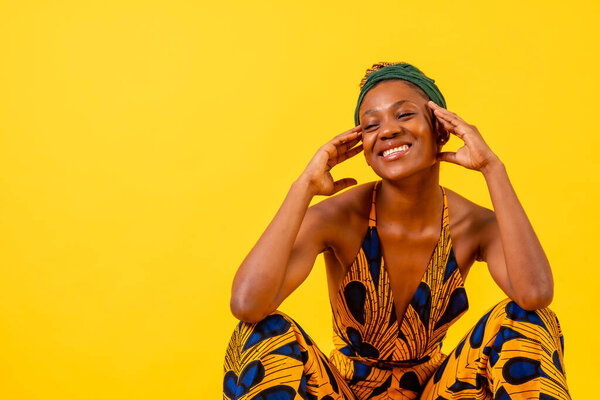 One black ethnic woman in traditional costume on yellow background, sitting, smiling