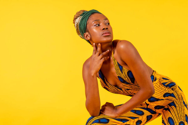 A female person of black ethnicity with traditional costume on yellow background, posed in fashion