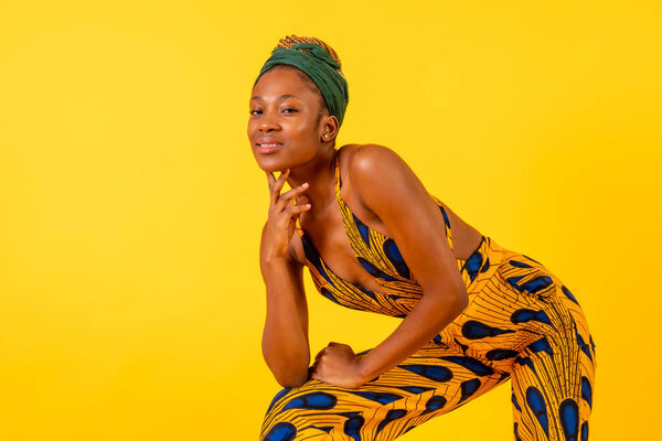 One person woman of black ethnicity with traditional costume on yellow background, sitting smiling