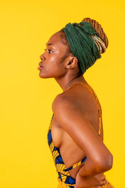 One female person of black ethnicity in traditional costume on yellow background, serious profile model