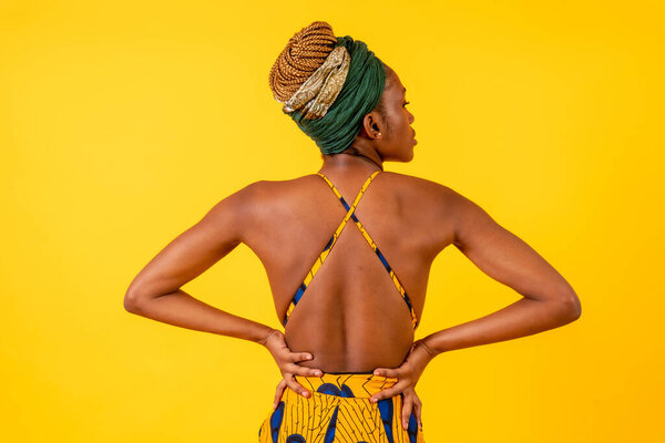 A person woman of black ethnicity with traditional costume on yellow background, model with a bare back