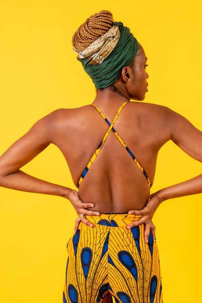 A person woman of black ethnicity with traditional costume on yellow background, model with a bare back