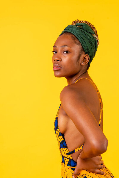 A person woman of black ethnicity with traditional dress on yellow background, profile model looking