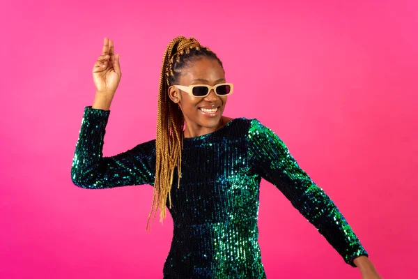 A black ethnic woman with braids dancing at party on a pink background, ballerina in a sequined dress