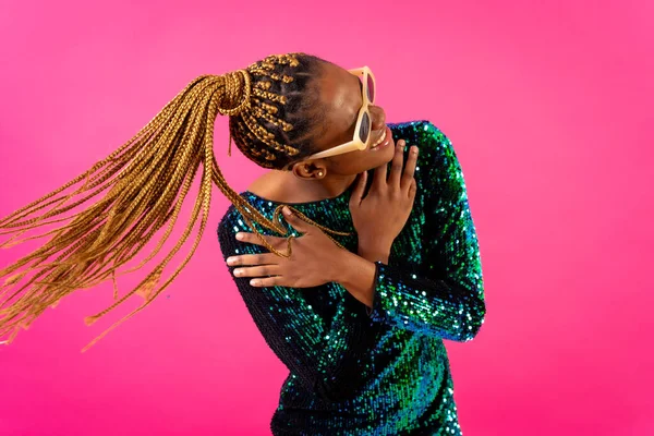 African young woman with party braids on a pink background, having fun dancing moving her hair