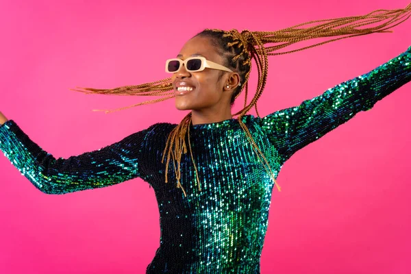 African young woman with party braids on a pink background, having fun dancing moving her hair
