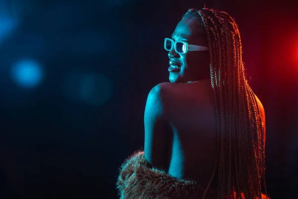 Black ethnic woman with braids with blue and red led lights, model from the back, sensual pose looking