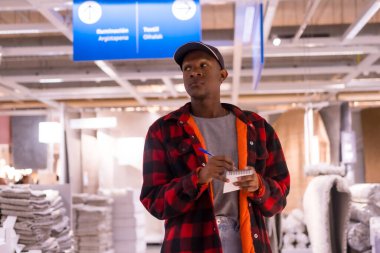 Siyahi bir adam halı süpermarketinde alışveriş yapıyor, fiyatlara bakıyor.