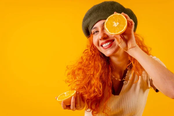 Руда Жінка Тримає Апельсин Над Ізольованим Жовтим Тлом Підморгуючи Фруктами — стокове фото