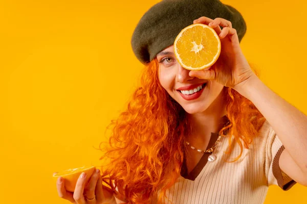 Руда Жінка Тримає Апельсин Над Ізольованим Жовтим Тлом Підморгуючи Фруктами — стокове фото