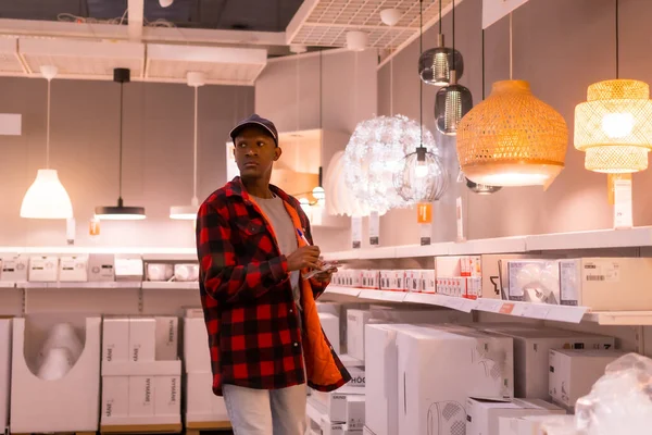 stock image Black ethnic man shopping in a supermarket for lamps, with the shopping list