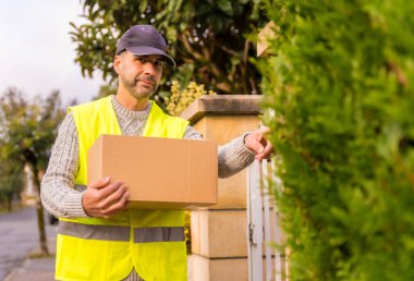 Çevrimiçi bir mağazadan gelen bir kutuyla paket teslimatçısı, zili çalıyor, boşluğu kopyalıyor