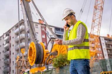 Site yöneticisi ve teknik mühendis şehir inşaat alanını inceliyor, telefonda konuşuyorlar.