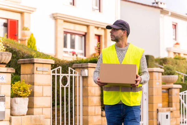 stock image Package delivery carrier from an online store, with a box in hand looking for the customer