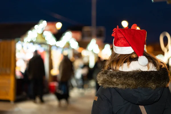 Woman from behind with christmas hat in the city at night, in a christmas market