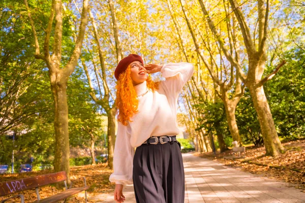 Red-haired woman with beret in a park, city forest at sunset, smiling