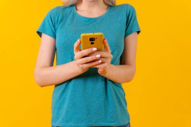 Ellerinde telefonla gülümseyen, sarı arka planda sarışın, beyaz bir kız.