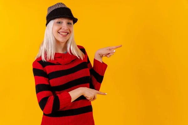 Pointing right with copy space, blonde caucasian girl on yellow studio background