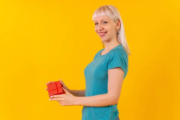 Delivering a surprise gift, blonde caucasian girl in studio on yellow background