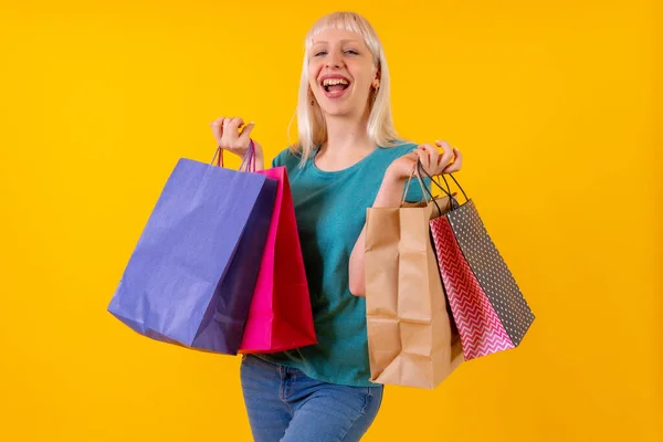 Laughing shopping with bags on sale, blonde caucasian girl in studio on yellow background