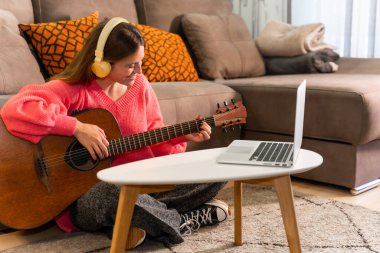 Evde gitar çalmayı öğrenen bir kadın. İnternette müzik notalarını takip eden bir kadın.