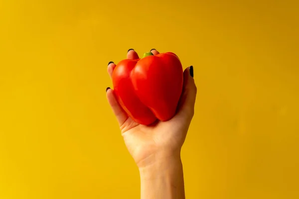 Woman's hand with a vegetable on a yellow background, healthy life, a red cucumber