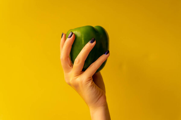 Woman's hand with a vegetable on a yellow background, healthy life, a green cucumber