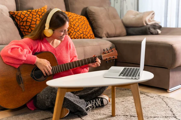 Woman learning to play the guitar at home with online classes on the computer, following the sheet music