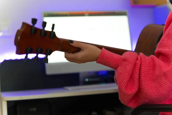 Caucasian woman learning to play the guitar with online classes on the computer