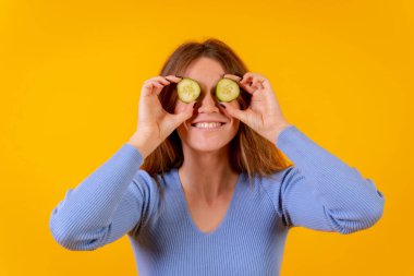 Gözlerinde salatalık dilimleri olan vejetaryen bir kadın sarı arka planda, vejetaryen hayatı
