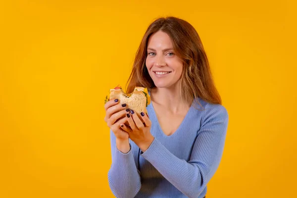 Vegetarian woman eating a sandwich on a yellow background, healthy vegetarian food
