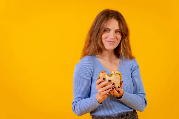 Vegetarian woman holding a sandwich on a yellow background, healthy vegetarian food