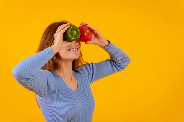 Vegetarian woman with spyglasses of peppers on her eyes on a yellow background, sticking out her tongue