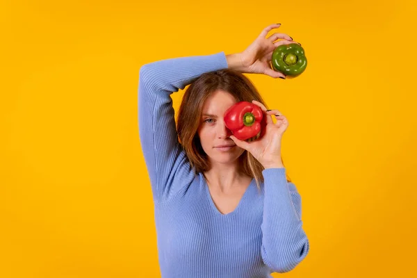 Portrait of vegetarian woman with green and red bell peppers on a yellow background, healthy food