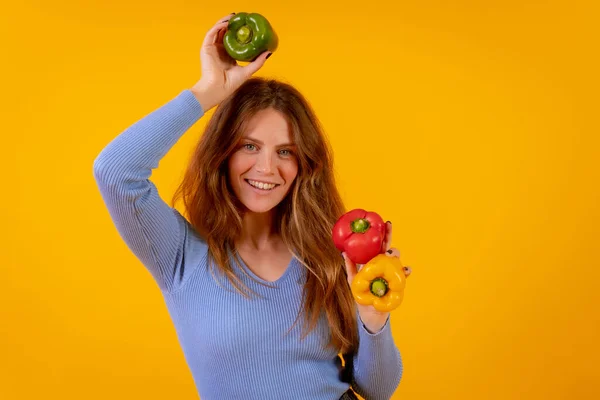 Vegetarian woman with green, yellow and red bell peppers on a yellow background, healthy food