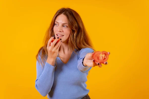 Vegan woman smiling holding a cut tomato on a yellow background
