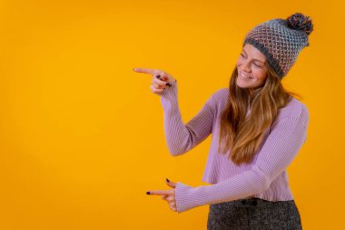 Sarı arka planda yün şapkalı bir kadın solu işaret ediyor, boşluğu kopyala