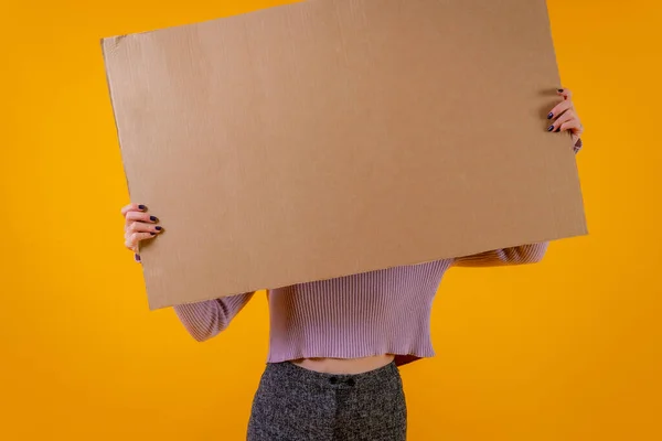 A cardboard sign held by a woman\'s hands on a yellow background